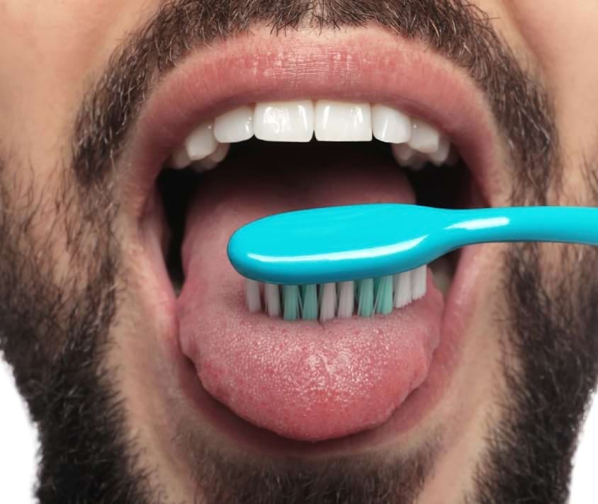 Muž si čistí zuby tyrkysovou zubnou kefkou.