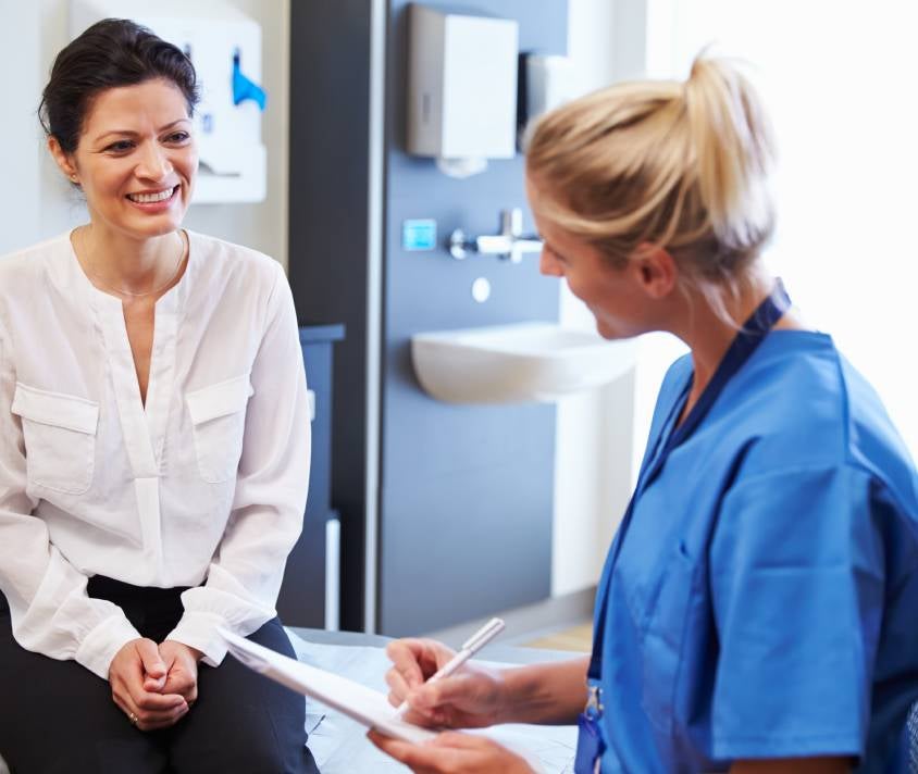 Mladá žena s okuliarmi si prezerá mobilný telefón v presvetlenej miestnosti s notebookom v pozadí.